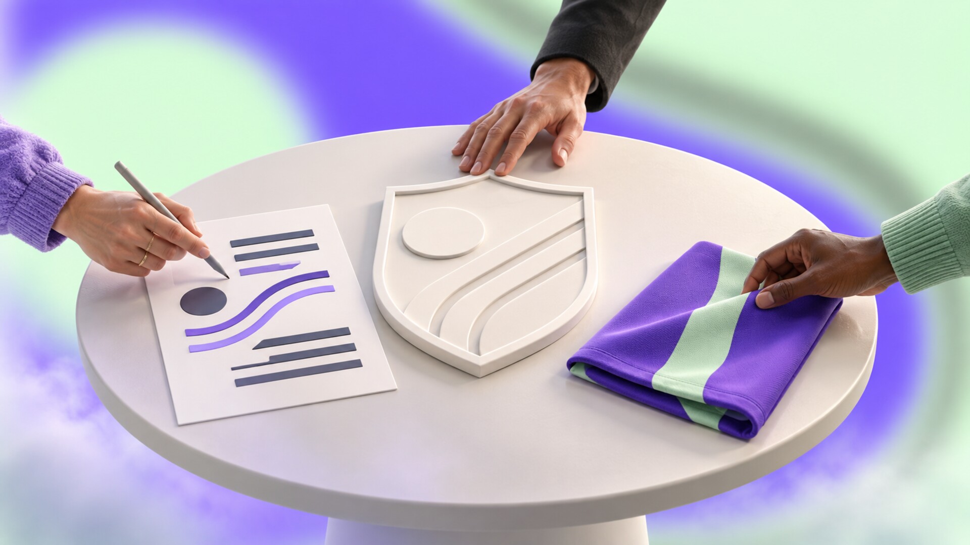 Three collaborators working around a round table with a blank shield model, graphic lines, and folded kit fabric.